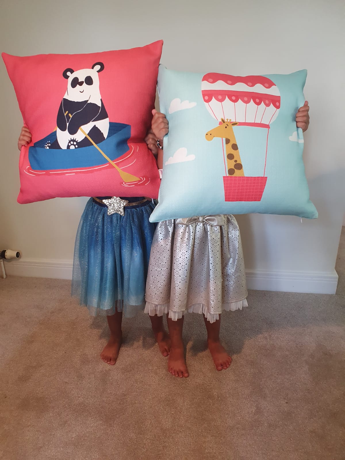 Two children holding decorative pillows with panda and giraffe designs against a plain background