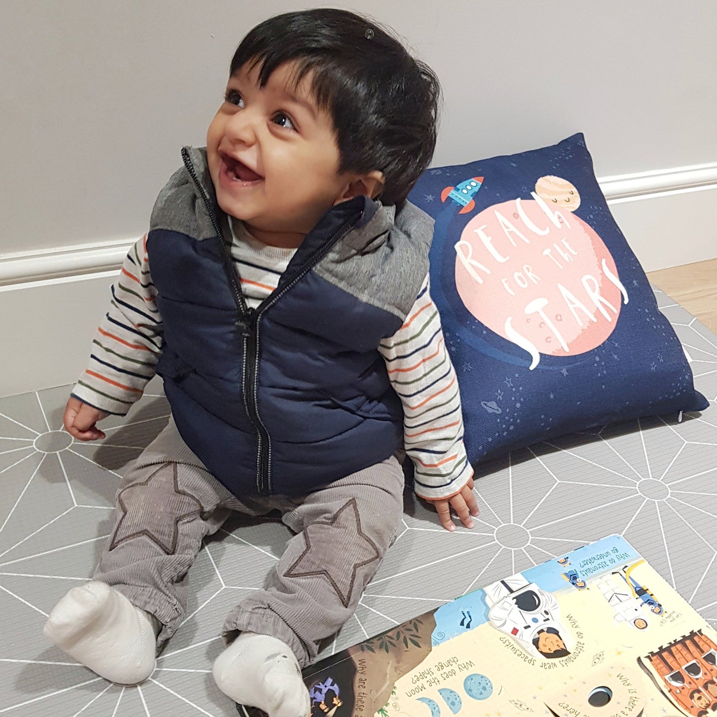 baby sitting next to space cushion with rocket ship, sleepy planets