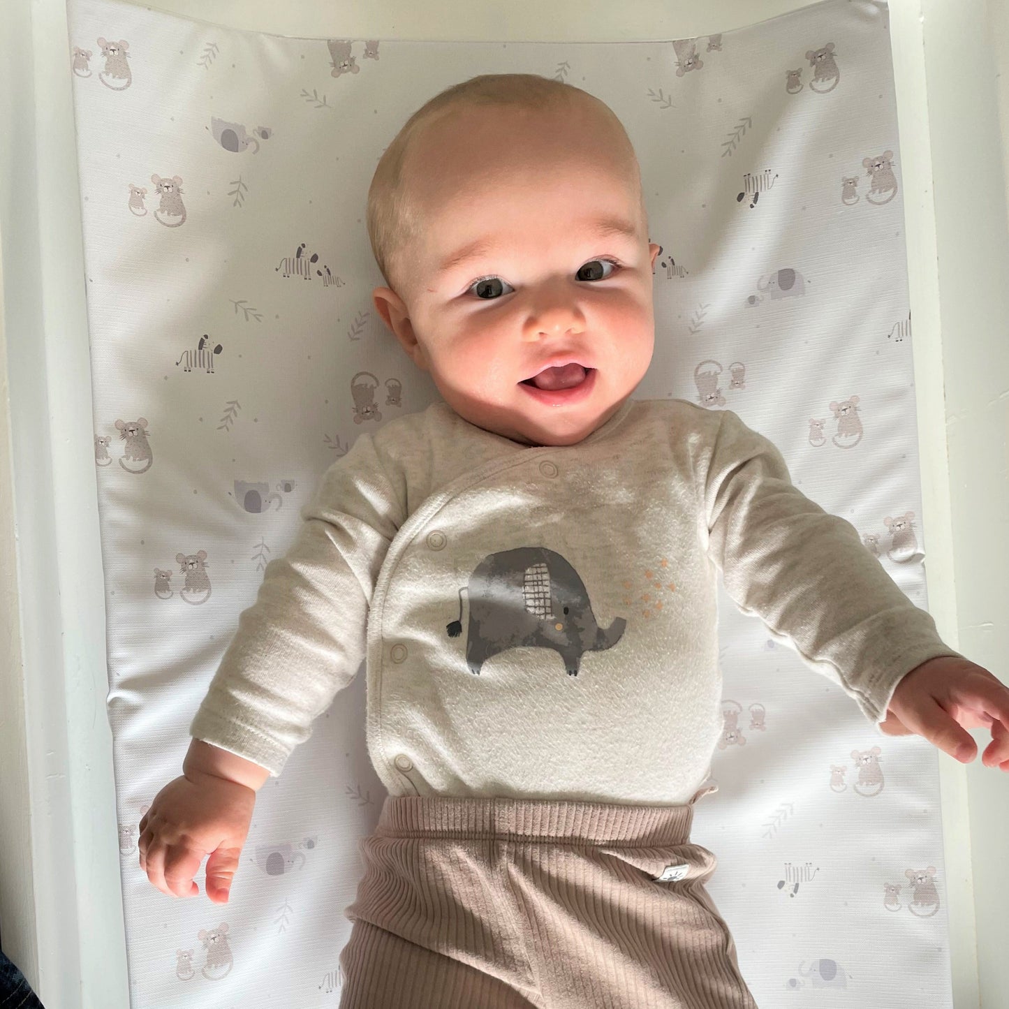 baby boy with elephant sleepsuit lying on a changing mat wih safari animals nursery