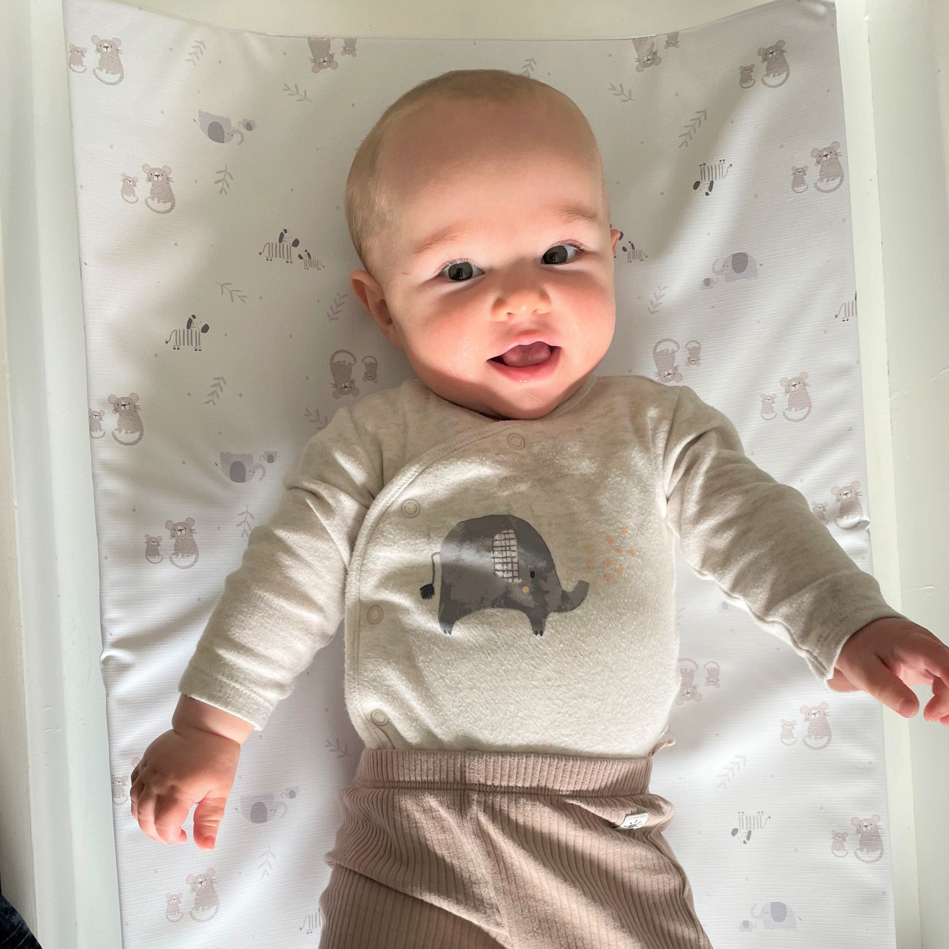 baby boy with elephant sleepsuit lying on a changing mat wih safari animals nursery